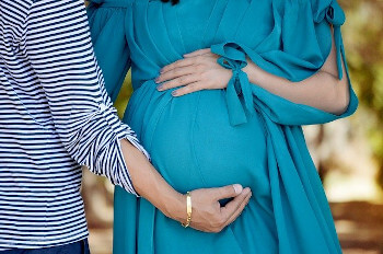 Eine schwangere Frau im Kleid und eine andere Frau halten den Babybauch der einen Frau