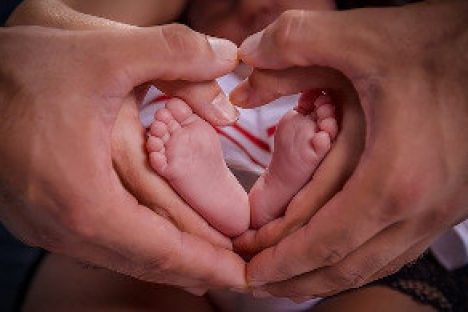 Die Hände der Eltern halten zwei Babyfüsse und formen dabei ein Herz